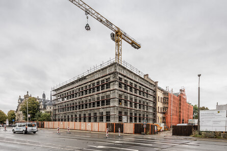 Außenaufnahme des vollständige eingerüsteten Gebäudes mit der Richtkrone am Krank hängend im Hintergrund.