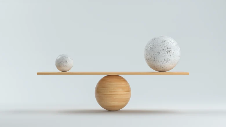 Holzwaage, die einen kleinen und einen großen Ball vor weißem Hintergrund balanciert