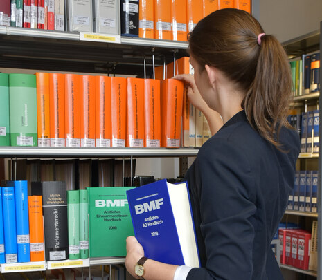 Beamtin sucht innerhalb eines Bücherregals nach Nachschlagewerken