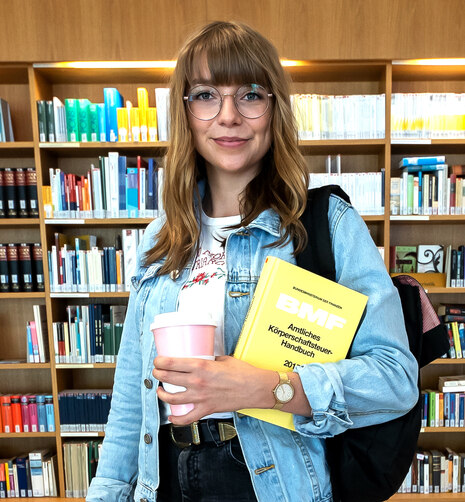 Junge Frau in der Bibliothek mit einer Mappe unterm Arm